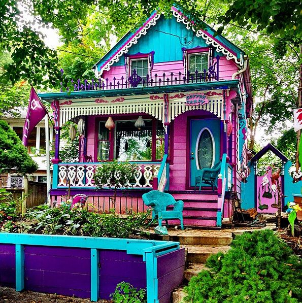 a pink and blue house sitting on top of a lush green field