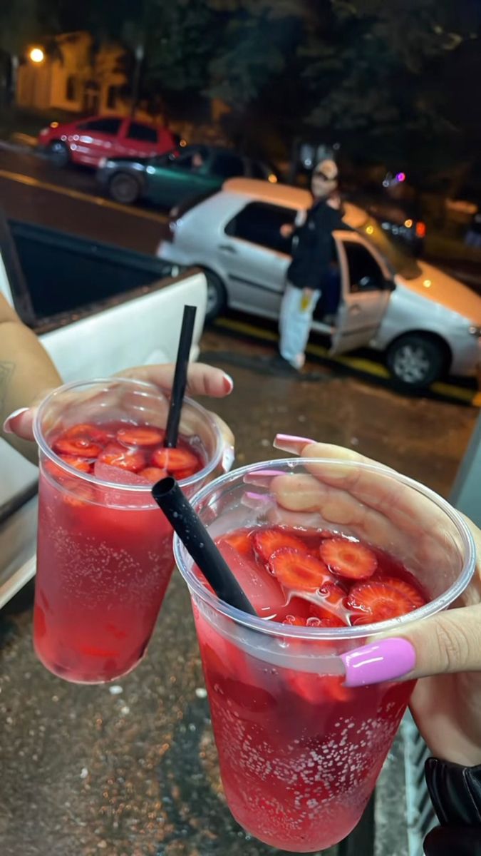 two people holding up drinks with strawberries in them