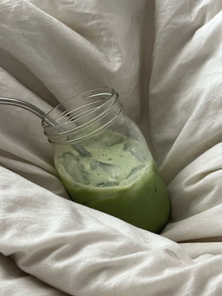 a jar filled with green liquid sitting on top of a white bed cover covered in sheets