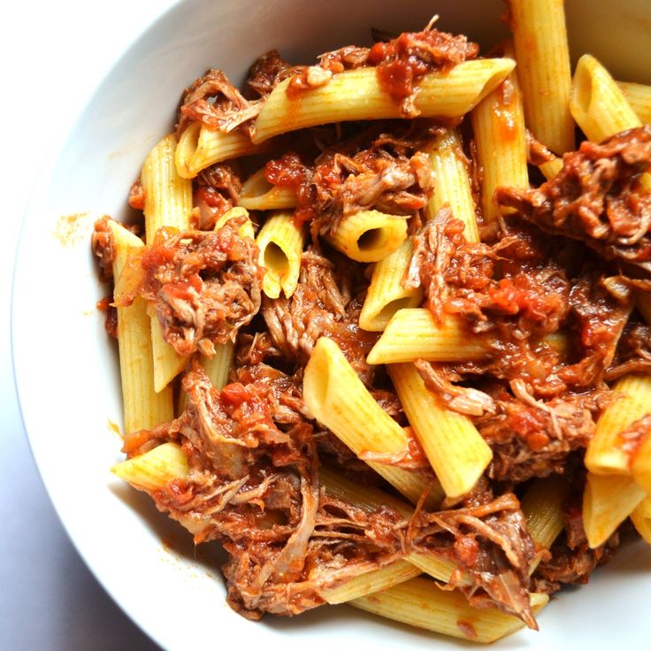 a white bowl filled with pasta covered in meat and marinara sauce on top of a table