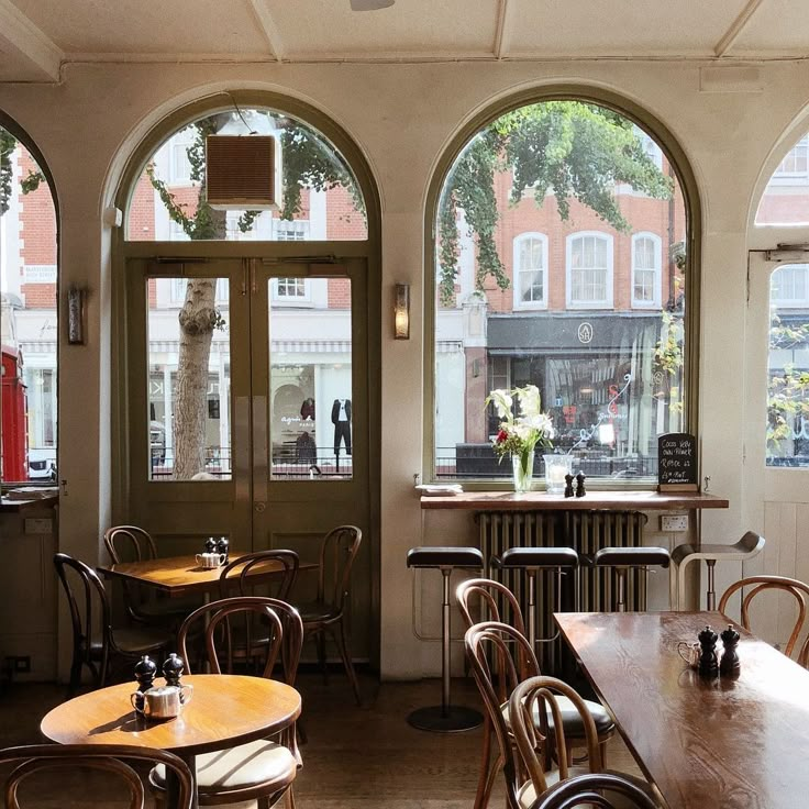 an empty restaurant with tables and chairs in front of large arched windows, looking out onto the street