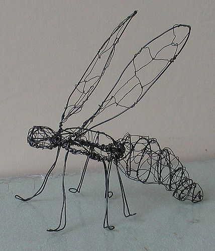 a wire sculpture of a dragonfly sitting on top of snow covered ground next to a white wall