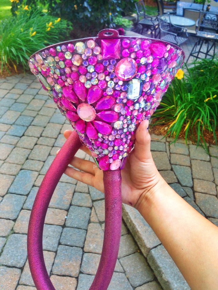 a hand holding up a purple vase with flowers on it's side and pink handles