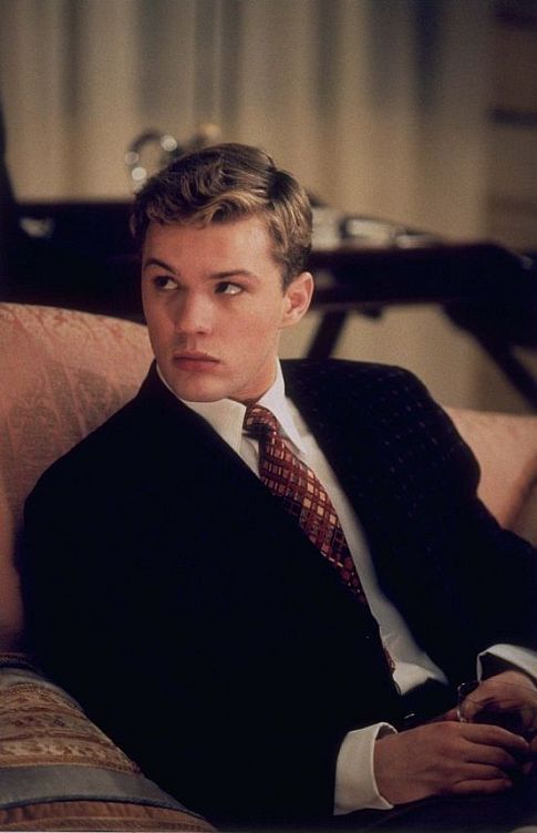 a young man in a suit and tie sitting on a couch looking at the camera