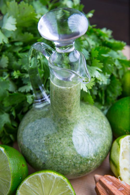 a glass bottle filled with green liquid next to limes and cilantro leaves