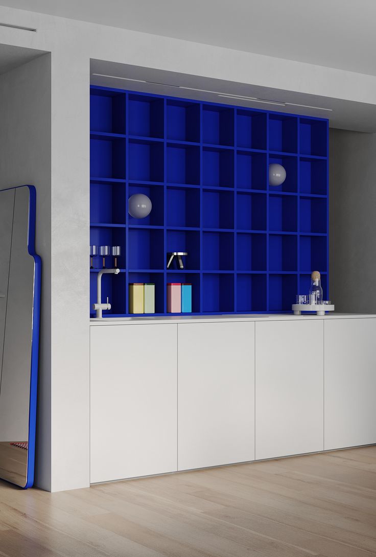 an empty room with blue bookshelves and white cabinets on the wall, in front of a mirror