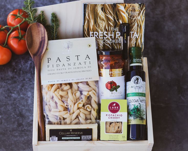 a wooden box filled with pasta, sauces and other food items next to tomatoes