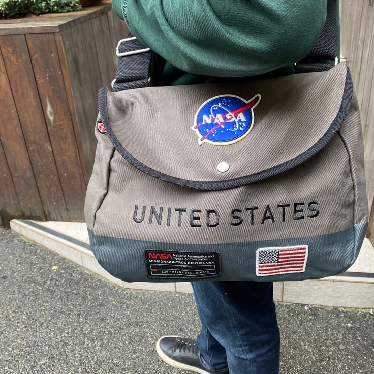 NASA Shoulder Bag From Red Canoe Introducing the NASA bag - the perfect choice for stylish and practical carrying. It is suitable for both everyday use and travel. On the front of the bag you can see the Nasa logo - felt patch, there is also Nasa embroidery on the side. The material of the bag is 100% cotton twill with an adjustable soft shoulder strap. Size: 35.5 cm Width 27.9 cm Height 8.9 cm Depth The NASA bag is a great gift for true space fans. Her stylish space design and connection with the Nasa company make her special. Outdoor Canvas Satchel Bag With Removable Pouch, Nasa Backpack, Nasa Embroidery, Nasa Merch, Nasa Aesthetic, Nasa Gifts, Nasa Patch, Felt Patch, Nasa Logo