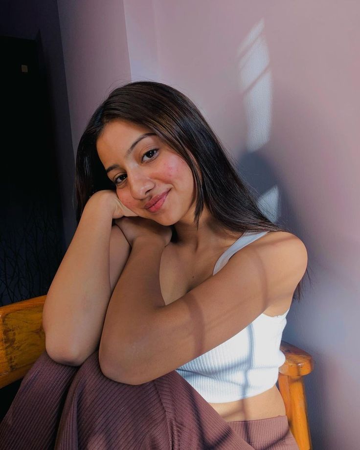 a woman sitting in a chair with her hand on her chin and looking at the camera