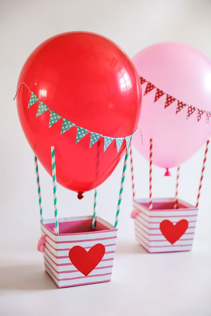 two red and pink balloons are in small boxes with flags on the top, one is filled with hearts