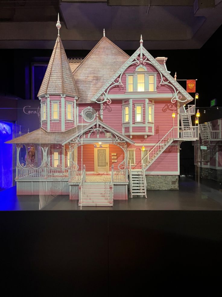 the doll house is pink and has white trim on it's sides, with stairs leading up to the second floor