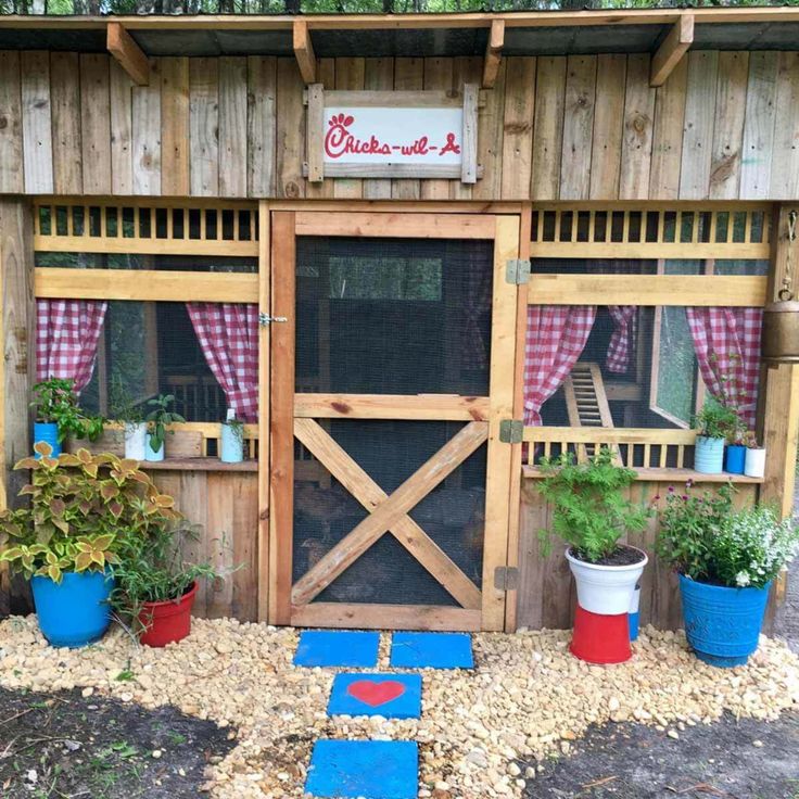 a small chicken coop in the woods with potted plants