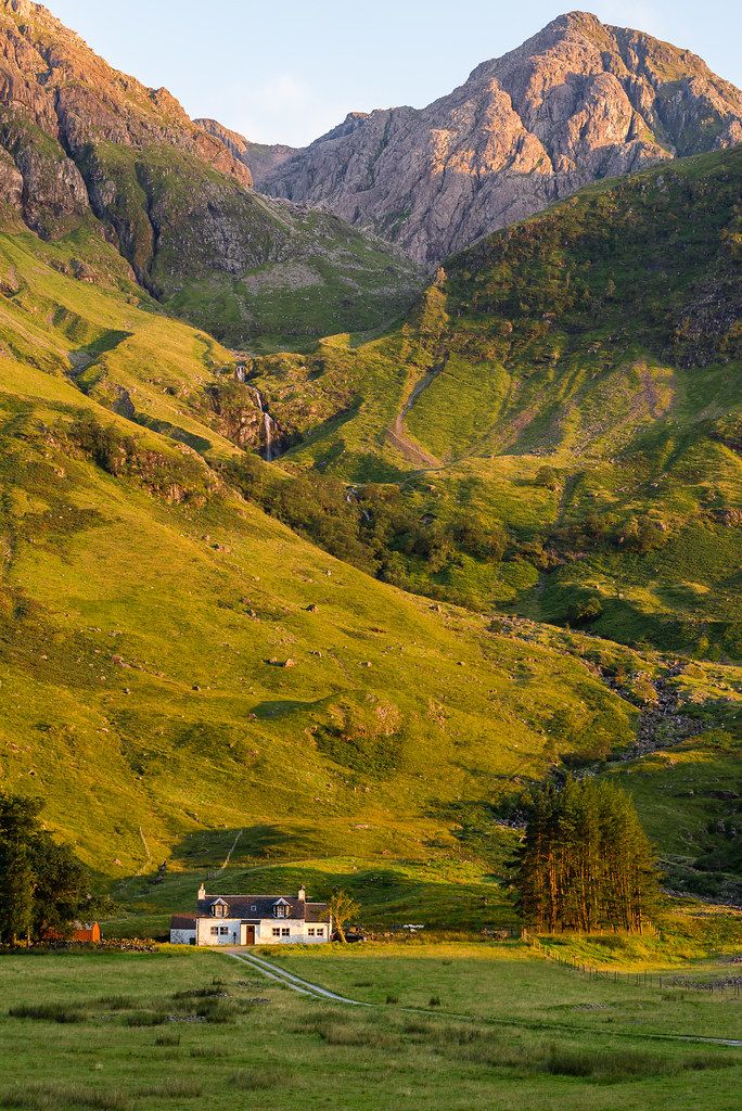 a house in the middle of a field with mountains in the background