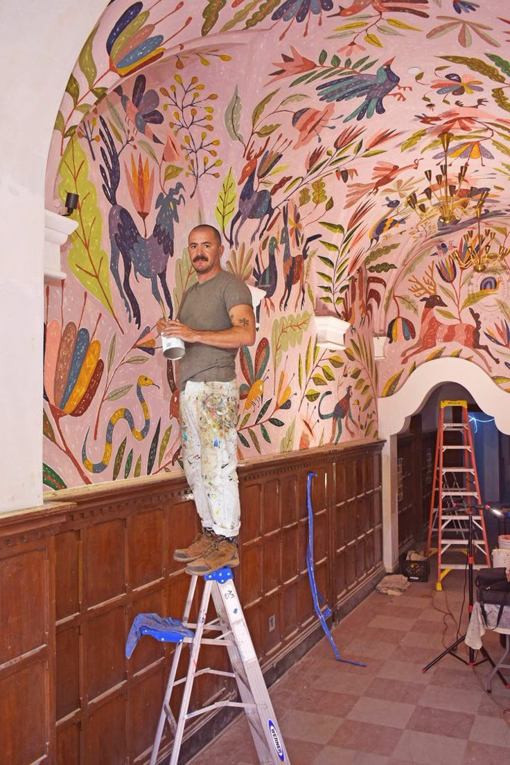 a man painting a mural on the side of a wall in a room with ladders