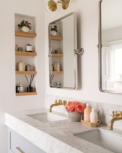 a bathroom with two sinks and gold faucets on the counter top, along with open shelving