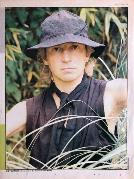 a young man wearing a hat and black shirt standing in tall grass with his hands on his hips