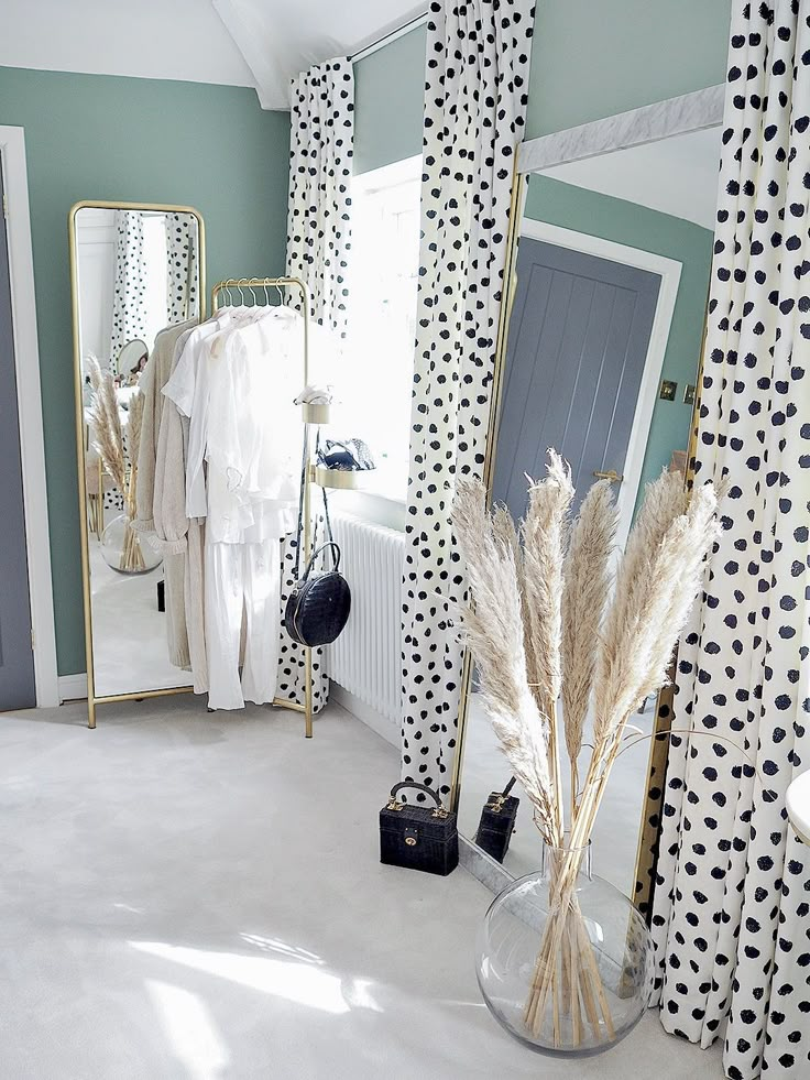 a room with black and white curtains, polka dot curtains, and a vase filled with dry grass