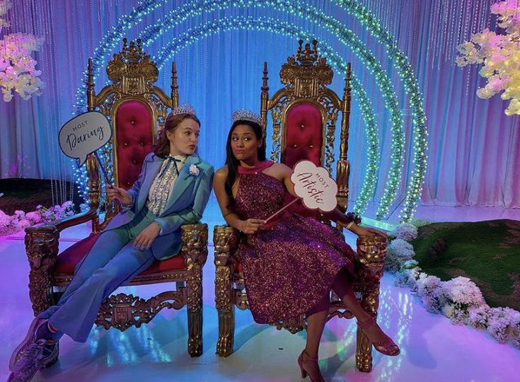 two women sitting on red chairs in front of a blue and white backdrop with flowers