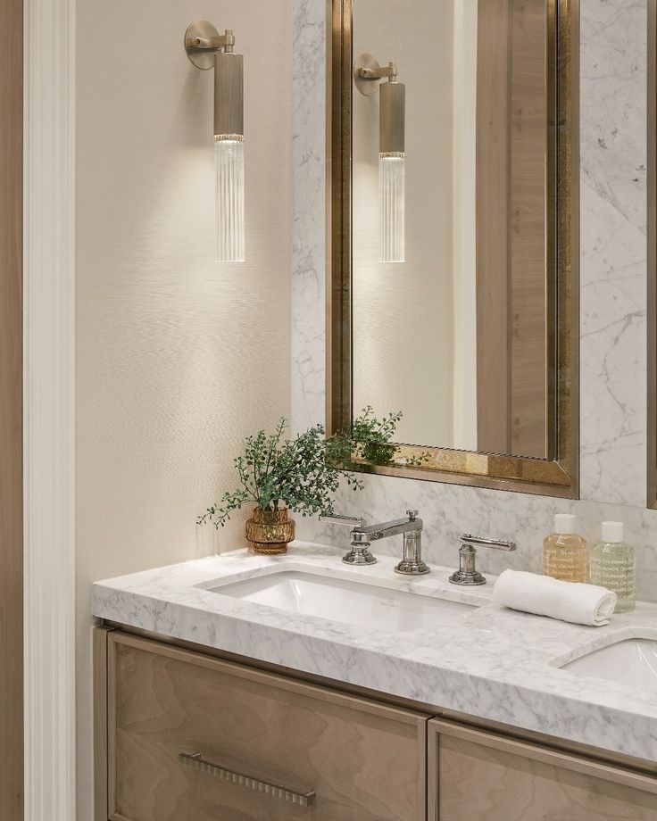 a bathroom with marble counter tops and two mirrors on the wall, along with a plant in a vase