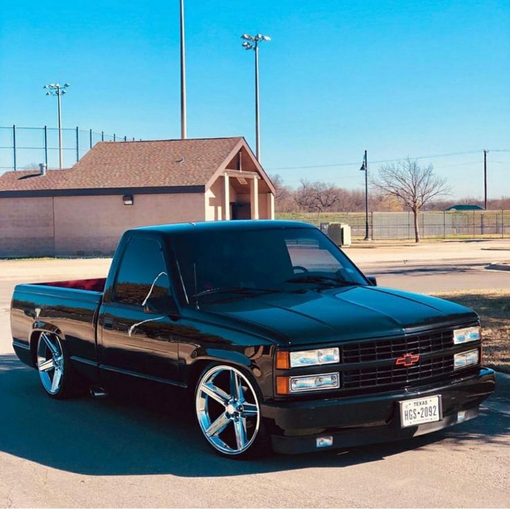 a black pickup truck parked in front of a building with blue rims on it's tires