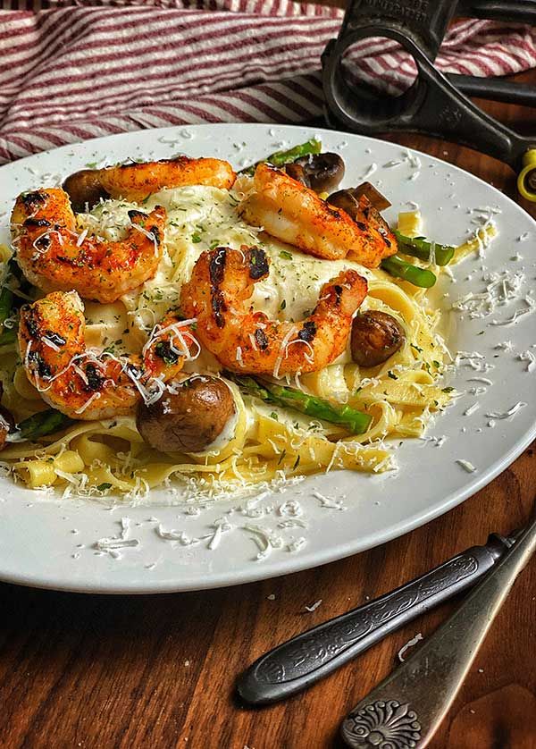 pasta with shrimp and mushrooms on a white plate next to utensils, fork and knife