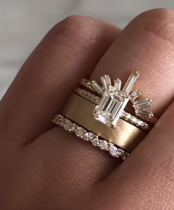 a woman's hand with two gold rings and an emerald ring on top of her finger