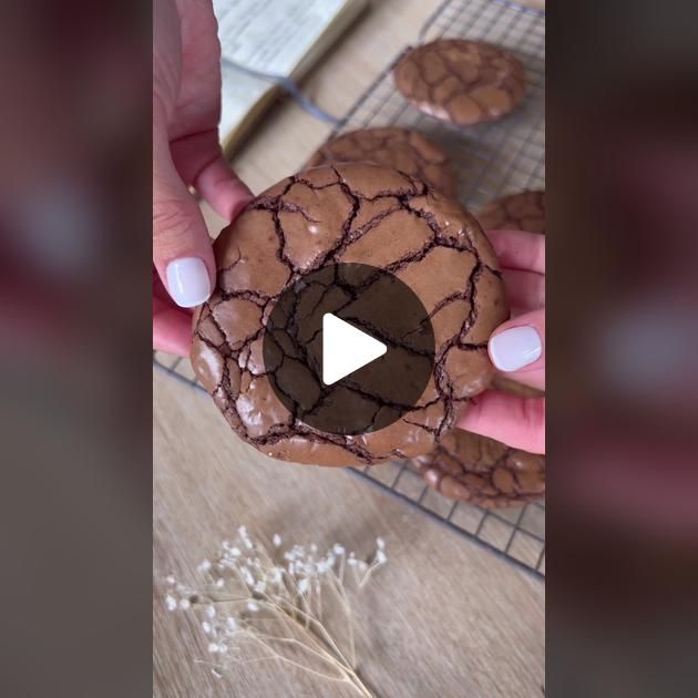 a person holding a chocolate donut on top of a cooling rack with white flowers