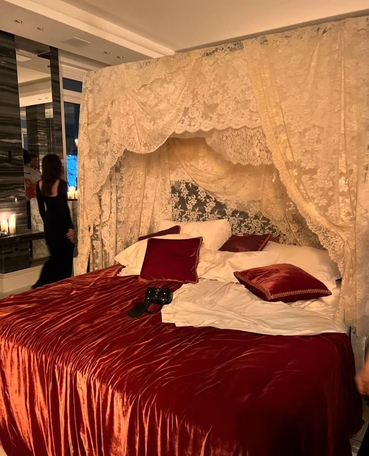 a woman standing next to a bed with red sheets and pillows on top of it