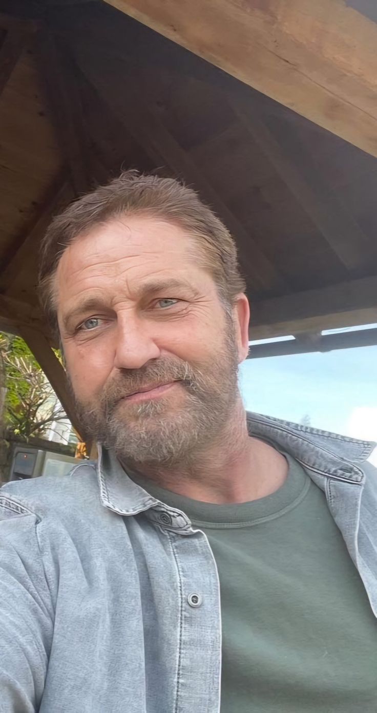 a man with a goatee and beard sitting under a wooden structure looking at the camera