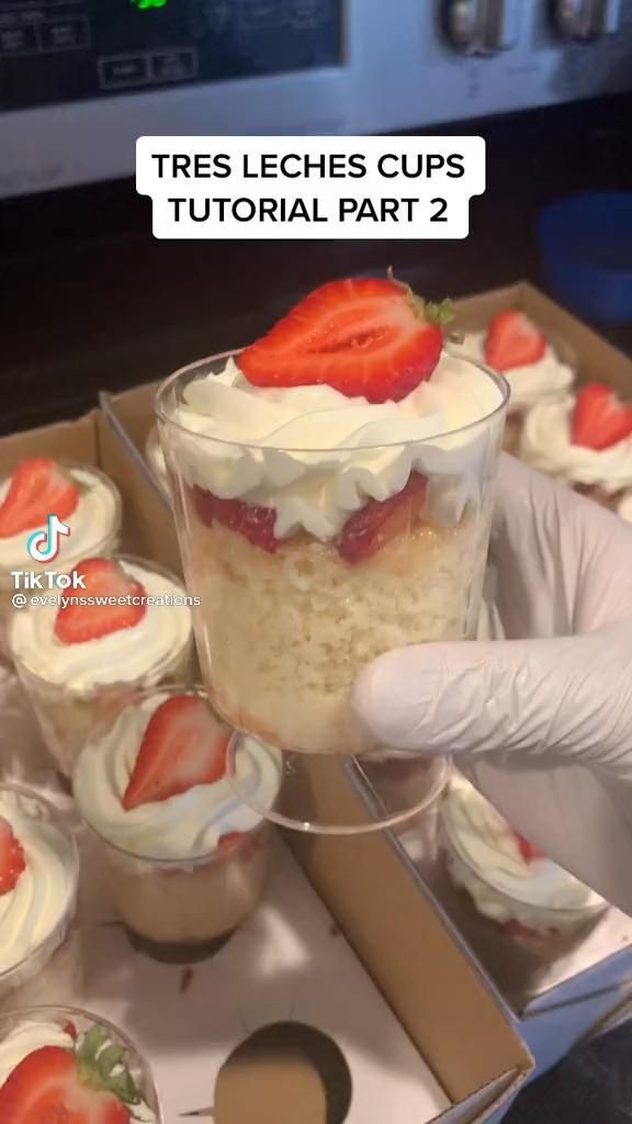 a person in white gloves holding up a dessert cup with strawberries on top and the words, tres leches cups tutorial part 2