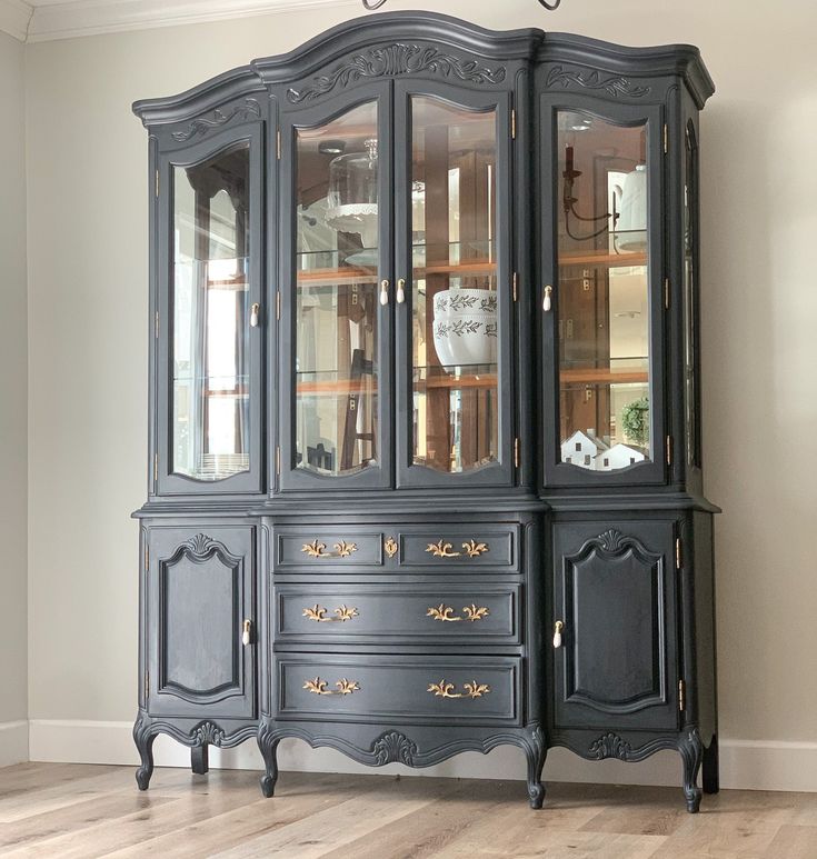 a black china cabinet with glass doors and gold trimmings on the bottom shelf