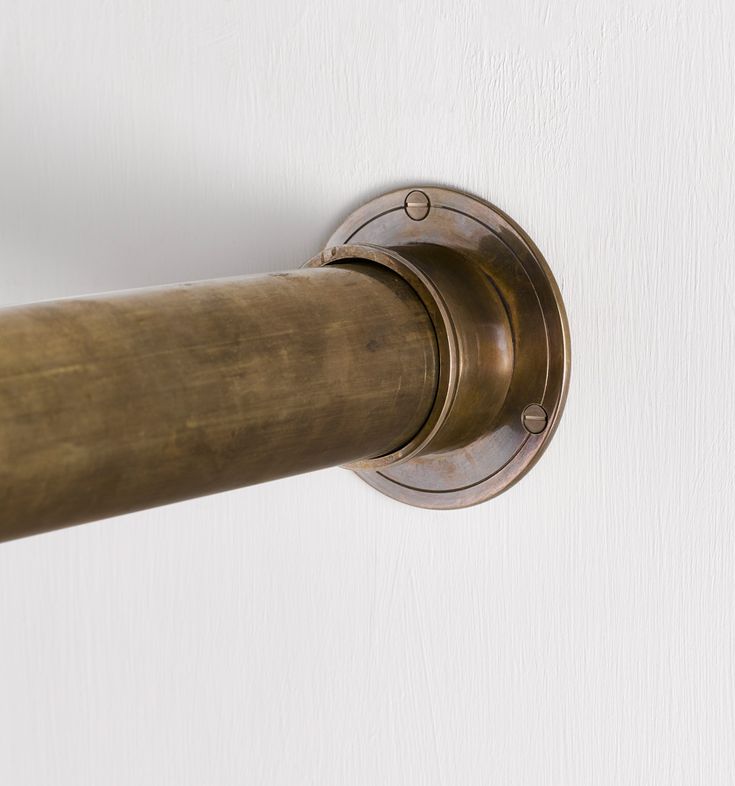 a close up of a metal pole on a white wall with a brown curtain rod