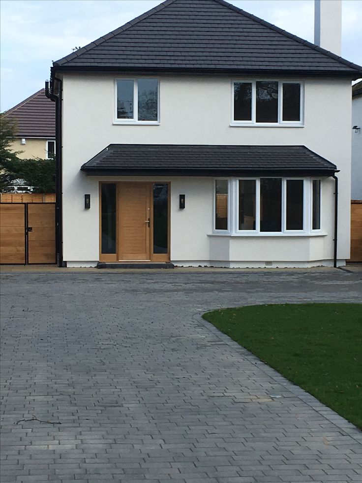 a large white house with a black roof and wooden gated driveway leading to the front door