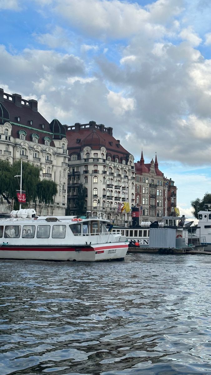 boats are docked on the water in front of large buildings and cloudy skies above them