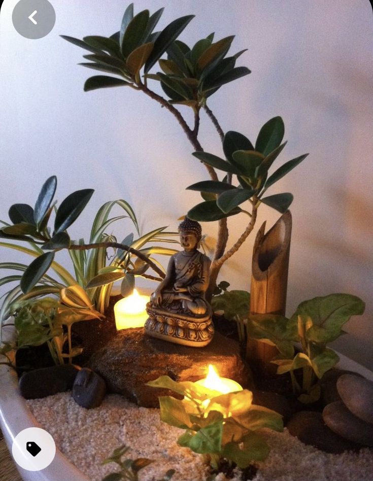 a small buddha statue sitting on top of a table surrounded by plants and rocks with lit candles