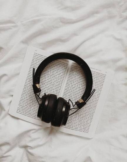 headphones on top of an open book laying on a white bed sheet with sheets