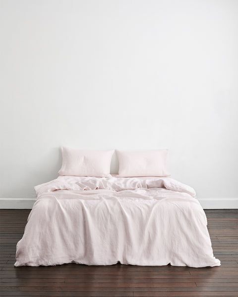 an unmade bed in a white room with wood flooring and pillows on it