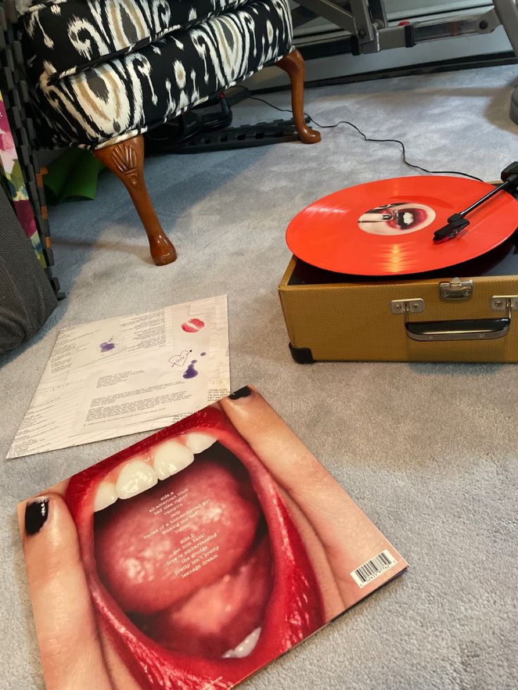 an open record player sitting on the floor next to a box with a red tongue