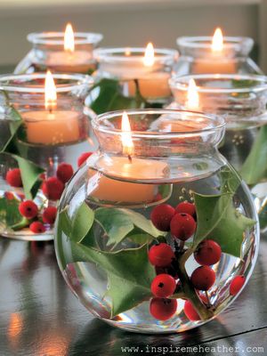 candles are lit in glass vases filled with holly and red berries