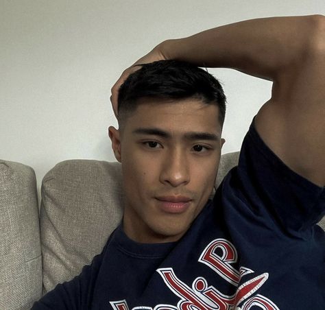 a young man sitting on top of a couch next to a white wall and holding his hands behind his head