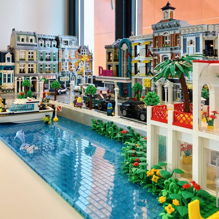 a lego model of a city with buildings and boats on the water in front of it