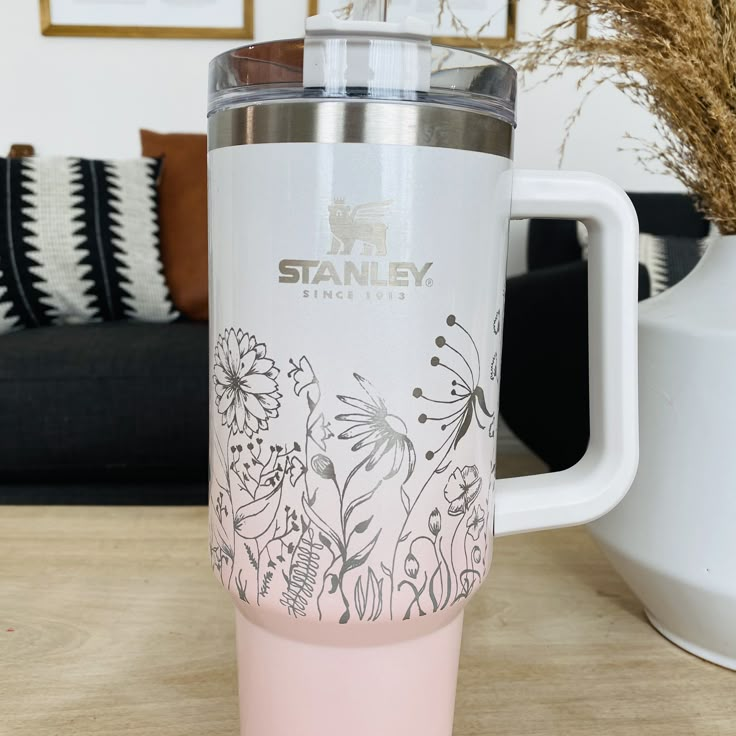 a pink tumbler cup sitting on top of a wooden table next to a vase