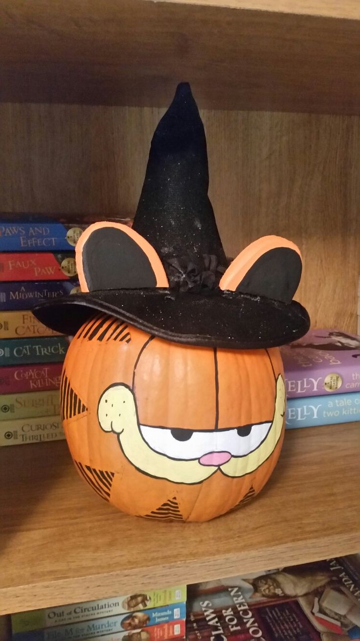 a pumpkin with a hat on top of it sitting on a book shelf next to books