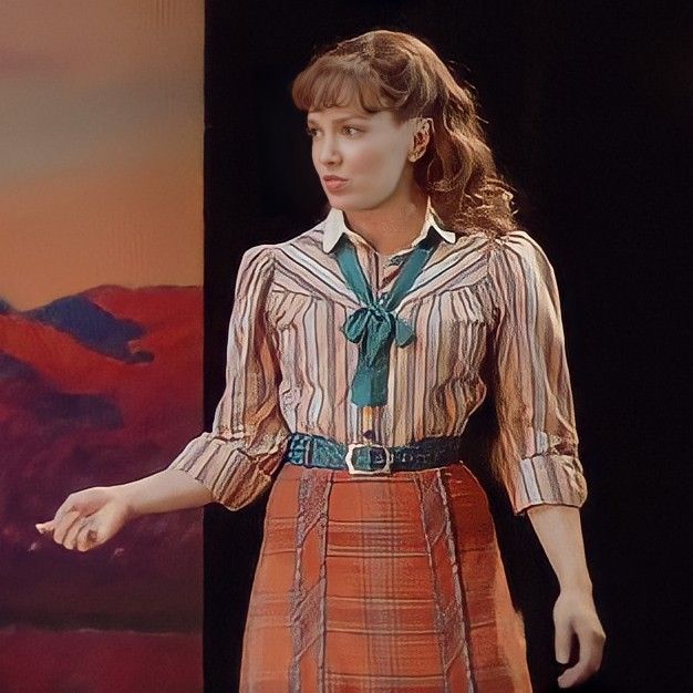 a woman standing in front of a painting with her hands out and wearing a skirt