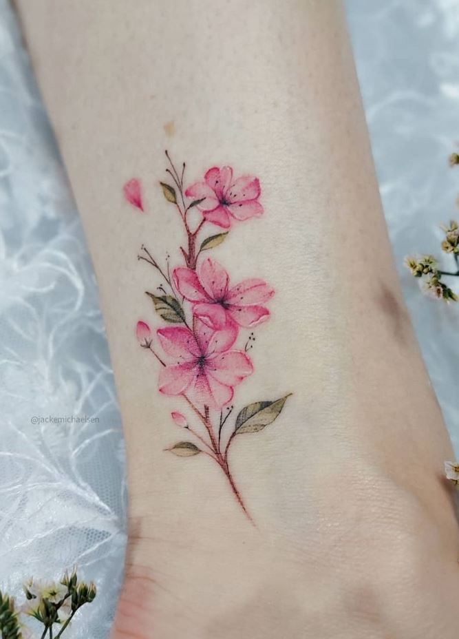 a small pink flower tattoo on the left side of the foot, with leaves and flowers around it