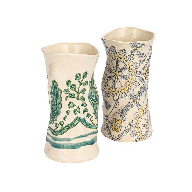 two ceramic vases sitting next to each other on a white surface with green and yellow designs