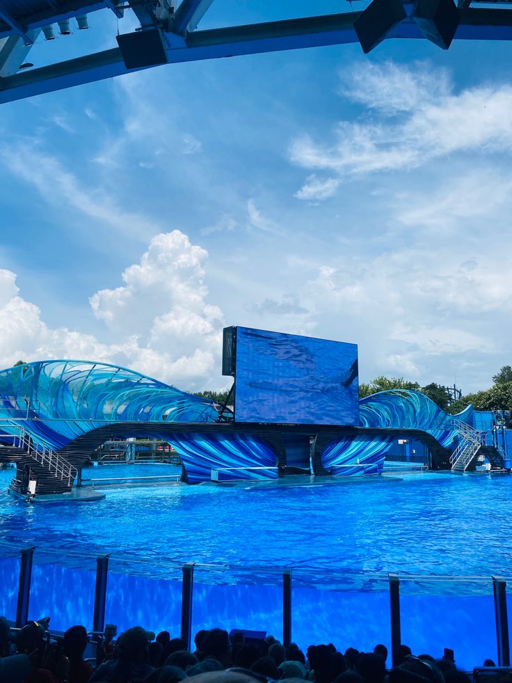 a large blue wave shaped structure sitting in the middle of a body of water with people watching