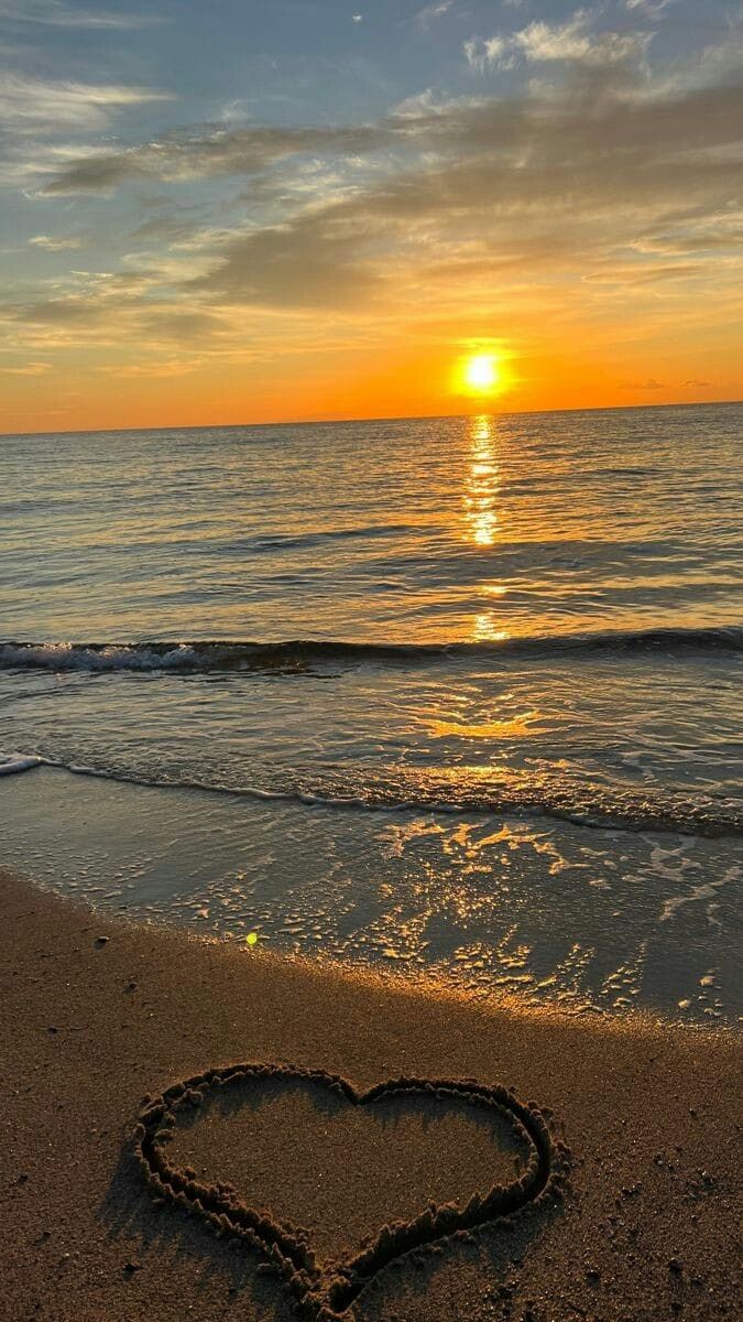 a heart drawn in the sand at sunset