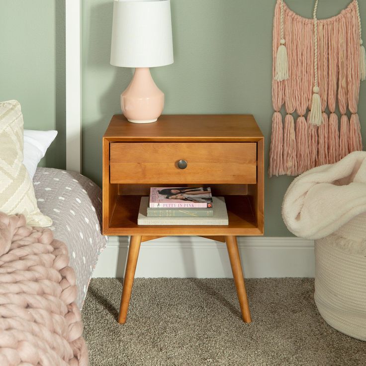 a nightstand with a lamp on it next to a bed and a pink throw pillow