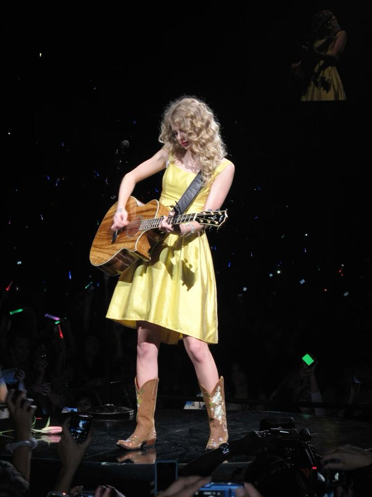 a woman in a yellow dress holding a guitar on stage with confetti flying around her